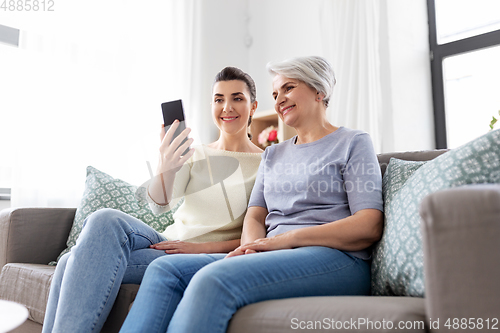 Image of senior mother with daughter taking selfie at home