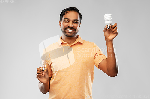 Image of smiling indian man comparing different light bulbs