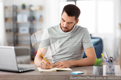 Image of man with notebook and laptop at home office