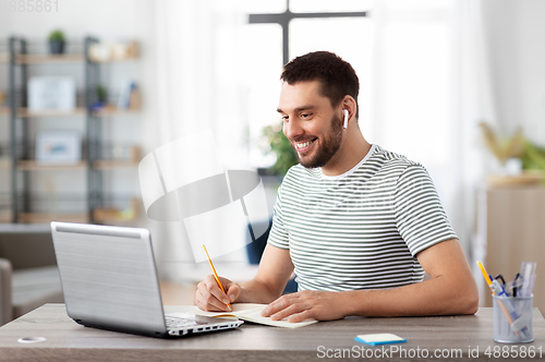 Image of man with notebook, earphones and laptop at home