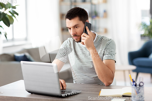 Image of man with laptop calling on phone at home office