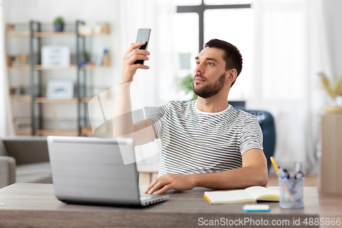 Image of man with smartphone and laptop at home office
