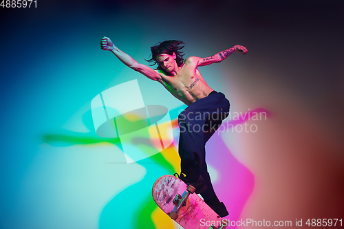 Image of Skateboarder doing a trick isolated on studio background in colorful neon light