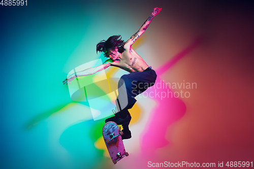 Image of Skateboarder doing a trick isolated on studio background in colorful neon light