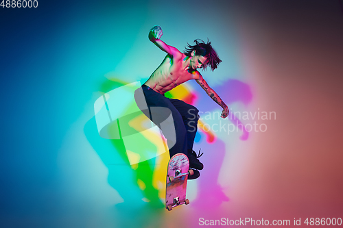 Image of Skateboarder doing a trick isolated on studio background in colorful neon light
