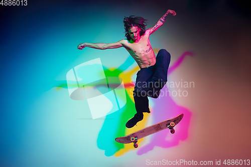 Image of Skateboarder doing a trick isolated on studio background in colorful neon light