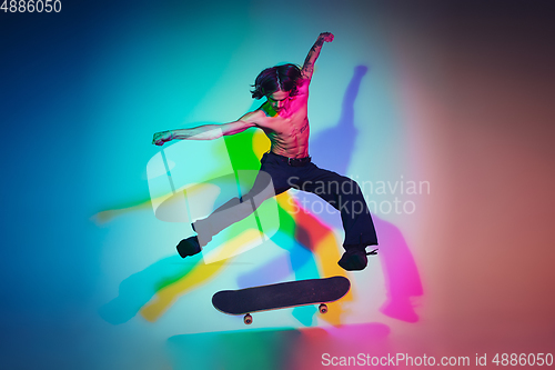 Image of Skateboarder doing a trick isolated on studio background in colorful neon light