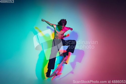 Image of Skateboarder doing a trick isolated on studio background in colorful neon light