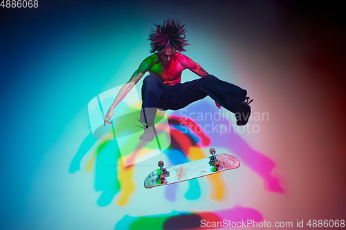 Image of Skateboarder doing a trick isolated on studio background in colorful neon light