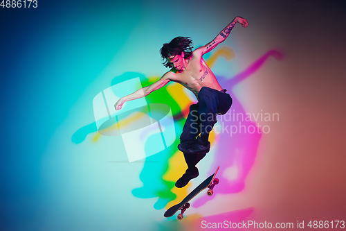 Image of Skateboarder doing a trick isolated on studio background in colorful neon light