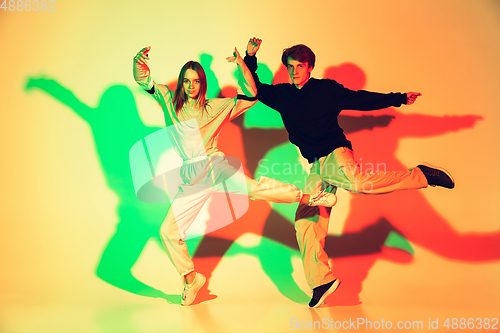 Image of Young man and woman dancing hip-hop, street style isolated on studio background in neon light