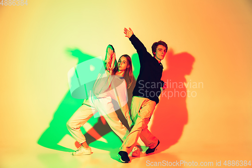 Image of Young man and woman dancing hip-hop, street style isolated on studio background in neon light