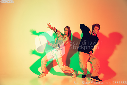 Image of Young man and woman dancing hip-hop, street style isolated on studio background in neon light