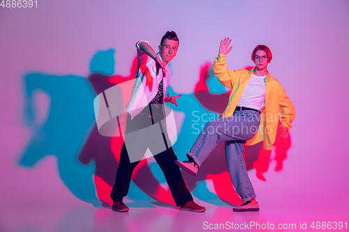 Image of Young man and woman dancing hip-hop, street style isolated on studio background in neon light