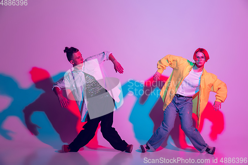 Image of Young man and woman dancing hip-hop, street style isolated on studio background in neon light