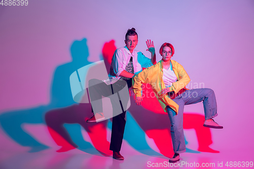 Image of Young man and woman dancing hip-hop, street style isolated on studio background in neon light