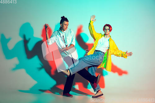 Image of Young man and woman dancing hip-hop, street style isolated on studio background in neon light