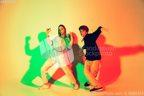 Image of Young man and woman dancing hip-hop, street style isolated on studio background in neon light