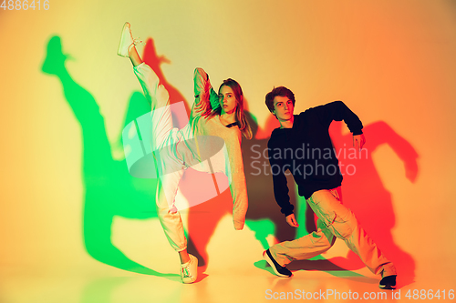 Image of Young man and woman dancing hip-hop, street style isolated on studio background in neon light