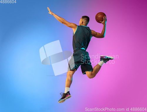 Image of Young basketball player in motion on gradient studio background in neon light