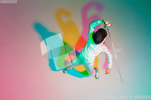 Image of Teen girl in fencing costume with sword in hand on gradient background with neon light, top view