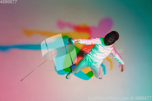 Image of Teen girl in fencing costume with sword in hand on gradient background with neon light, top view
