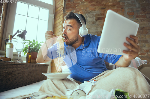 Image of Lazy man living the whole life in his bed surrounded with messy