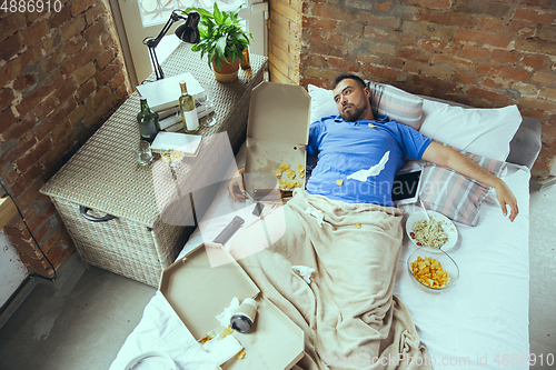 Image of Lazy man living the whole life in his bed surrounded with messy