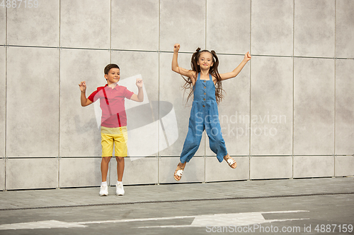 Image of Two smiling kids, boy and girl jumping together in town, city in summer day