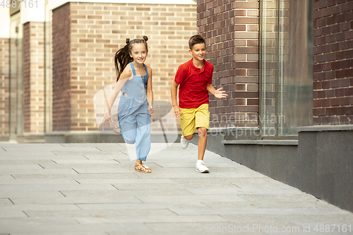 Image of Two smiling kids, boy and girl running together in town, city in summer day