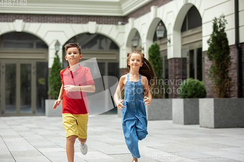 Image of Two smiling kids, boy and girl running together in town, city in summer day