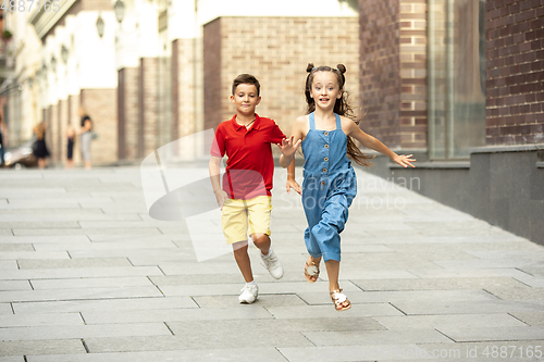 Image of Two smiling kids, boy and girl running together in town, city in summer day