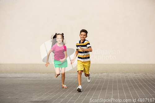Image of Two smiling kids, boy and girl running together in town, city in summer day