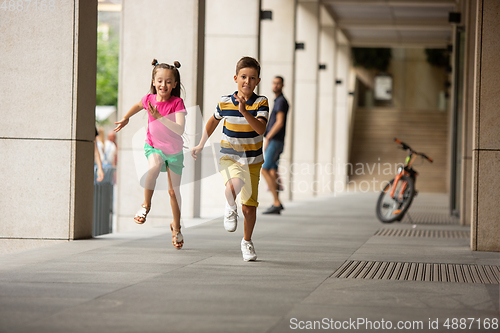 Image of Two smiling kids, boy and girl running together in town, city in summer day