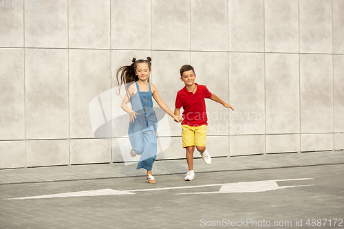 Image of Two smiling kids, boy and girl running together in town, city in summer day