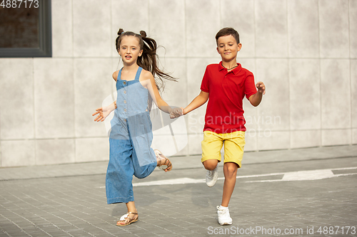 Image of Two smiling kids, boy and girl running together in town, city in summer day
