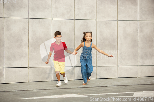 Image of Two smiling kids, boy and girl running together in town, city in summer day