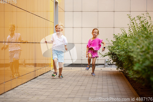 Image of Two smiling kids, boy and girl running together in town, city in summer day