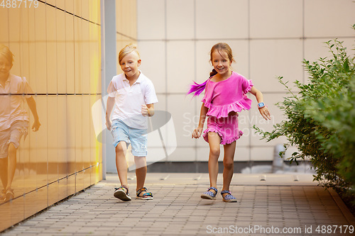 Image of Two smiling kids, boy and girl running together in town, city in summer day