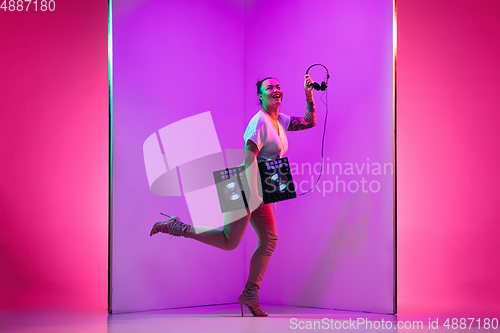 Image of Young caucasian female musician in headphones performing on purple background in neon light