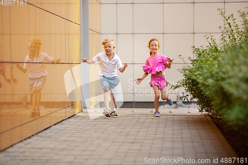 Image of Two smiling kids, boy and girl running together in town, city in summer day