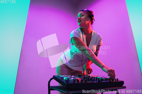 Image of Young caucasian female musician in headphones performing on purple background in neon light