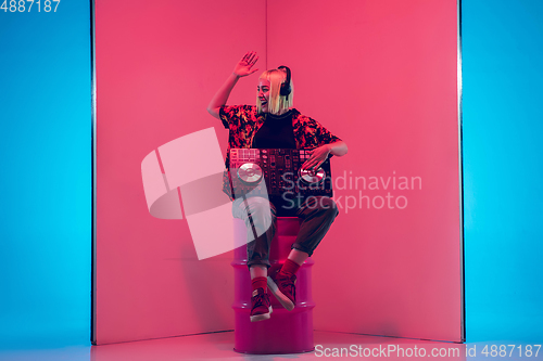 Image of Young caucasian female musician in headphones performing on blue-red background in neon light