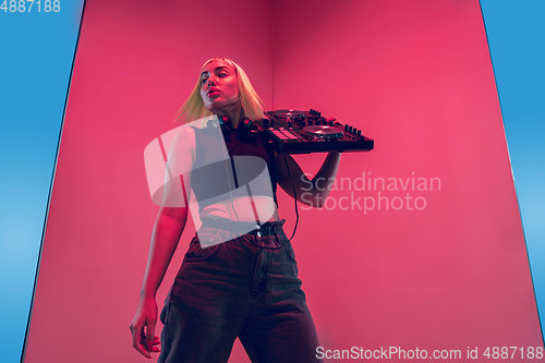 Image of Young caucasian female musician in headphones performing on blue-red background in neon light