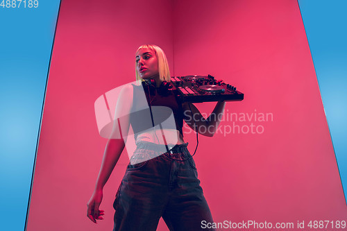 Image of Young caucasian female musician in headphones performing on blue-red background in neon light