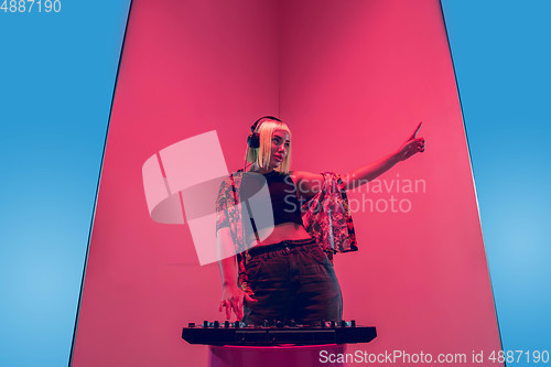 Image of Young caucasian female musician in headphones performing on blue-red background in neon light