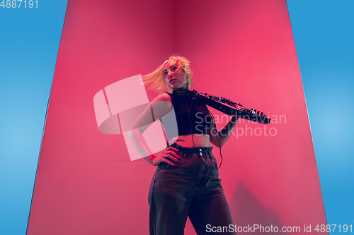 Image of Young caucasian female musician in headphones performing on blue-red background in neon light
