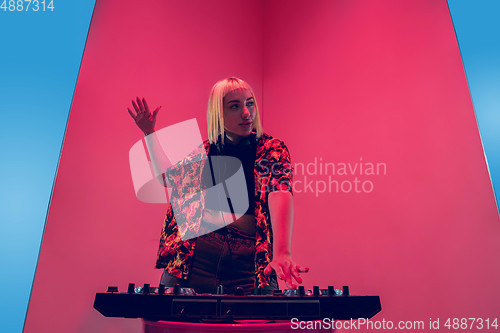 Image of Young caucasian female musician in headphones performing on blue-red background in neon light