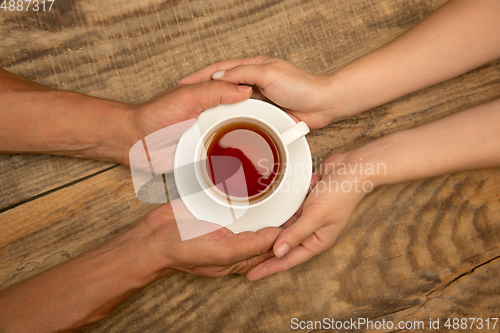 Image of Hands of couple holding mug of tea, top view on wooden background with copyspace