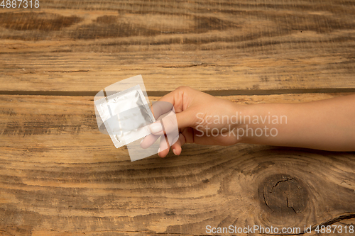 Image of Female hand holding condom isolated on wooden background